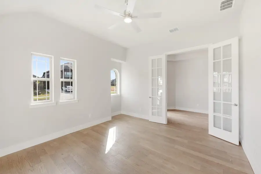Empty room with hardwood floors, ceiling fan, and white French doors leading to adjacent space