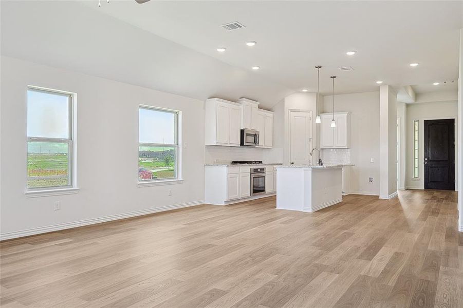 Kitchen with an island with sink, white cabinets, lofted ceiling, appliances with stainless steel finishes, and decorative light fixtures