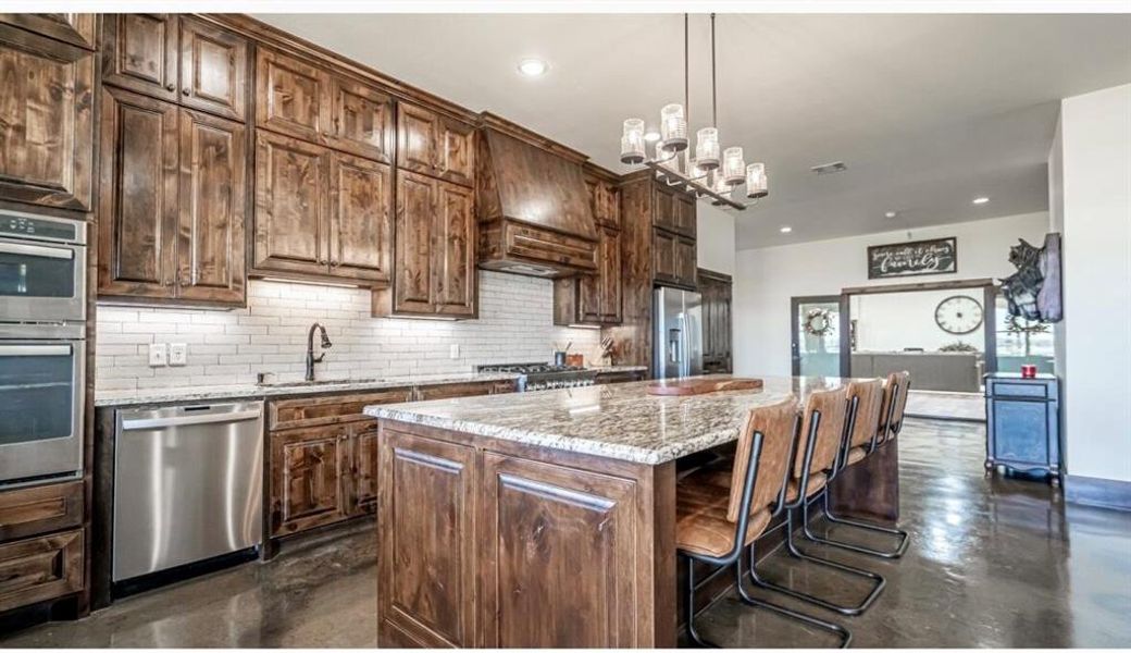 Kitchen with decorative backsplash, a breakfast bar area, finished concrete floors, light stone countertops, and a center island Kitchen with decorative backsplash, a breakfast bar area, finished concrete floors, light stone countertops, and a center island
