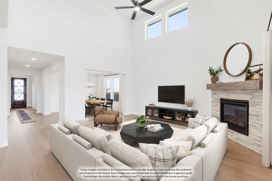 Open living room with two-story ceiling, stone fireplace, ceiling fan, and view to entry and dining area Open living room with two-story ceiling, stone fireplace, ceiling fan, and view to entry and dining area
