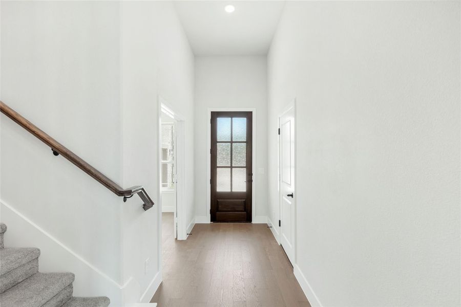 Bright entryway with dark wood front door, hardwood floors, high ceilings, and staircase with wood handrail. Bright entryway with dark wood front door, hardwood floors, high ceilings, and staircase with wood handrail.