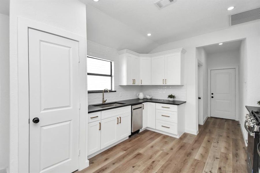 This is a modern, open-concept kitchen with white cabinetry, black countertops, and stainless steel appliances, leading into a dining area with abundant natural light.