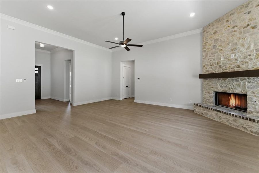 Spacious living area featuring a floor-to-ceiling stone fireplace with a dark wood mantel, light wood-finish flooring, recessed lighting, and a ceiling fan