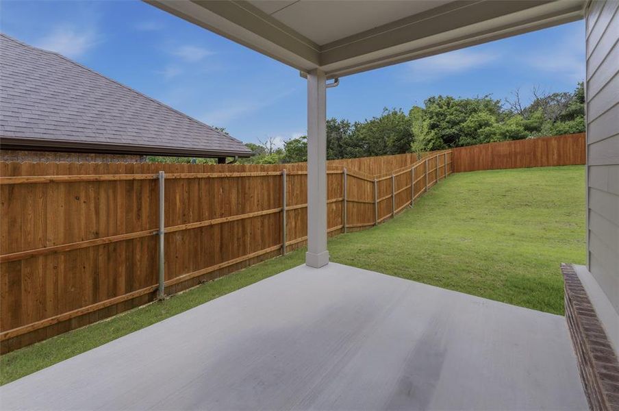 Covered concrete patio with a full wooden privacy fence and a spacious green lawn