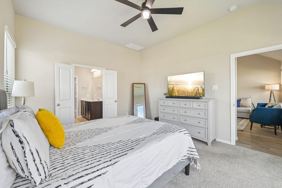 Spacious bedroom with soft, neutral tones, featuring a cozy bed, modern ceiling fan, and ample natural light. The room offers convenient access to an en-suite bathroom and a comfortable sitting area.