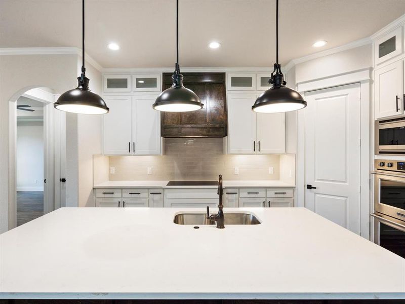 Kitchen featuring sink, white cabinetry, hanging light fixtures, a center island with sink, and ornamental molding