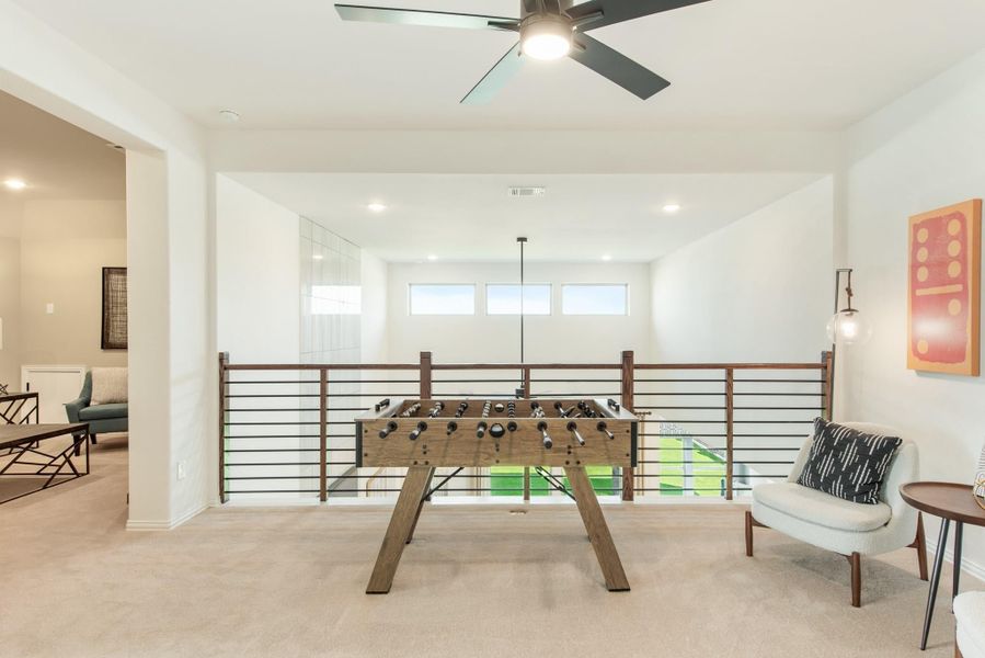 Open loft game room with foosball table, metal railing, ceiling fan, and carpet flooring Open loft game room with foosball table, metal railing, ceiling fan, and carpet flooring