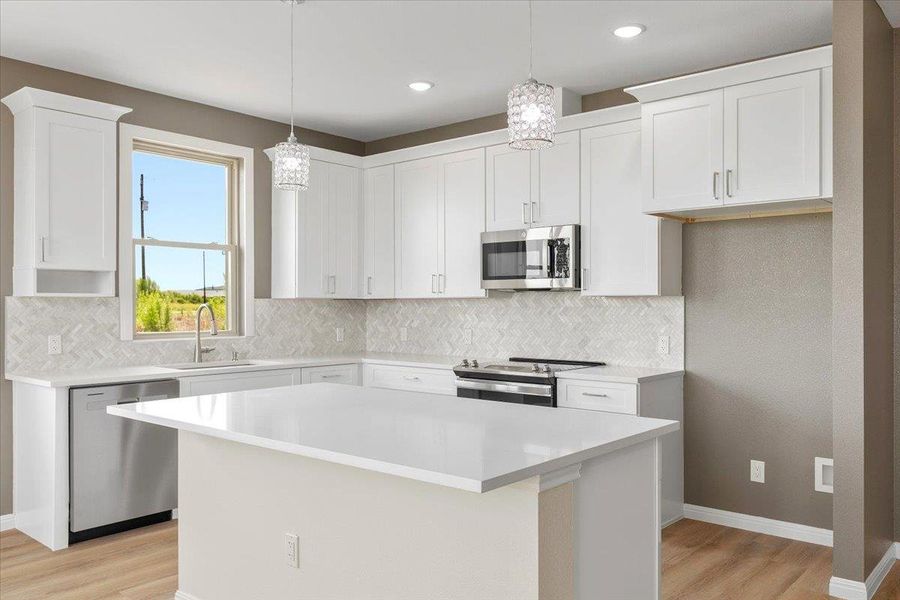 A pristine white kitchen featuring a large island, stainless steel appliances, and elegant pendant lighting. A pristine white kitchen featuring a large island, stainless steel appliances, and elegant pendant lighting.