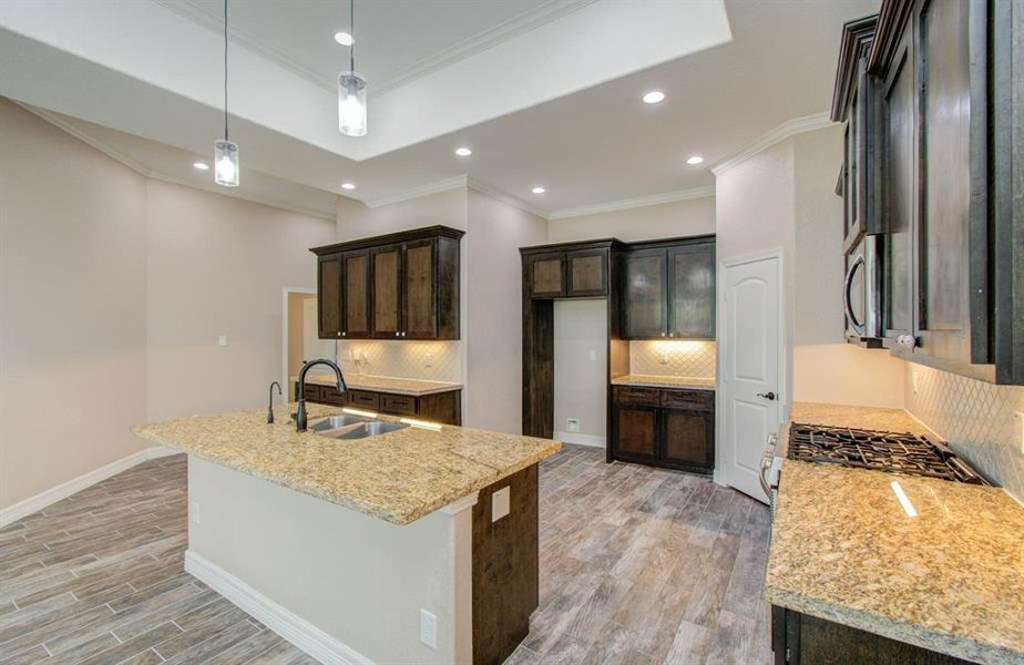 This is a modern kitchen with dark wood cabinets, granite countertops, and stainless-steel appliances, complemented by elegant pendant lighting and wood-look flooring.