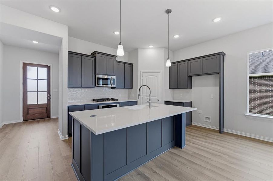 Kitchen featuring a central island with a gooseneck faucet, light countertops, dark cabinetry, and wood-finish flooring