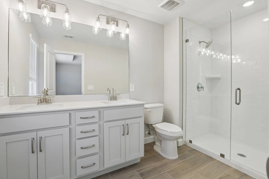 Luxurious primary bath with dual vanities and stunning frameless glass shower, featuring AW Collection® Milan