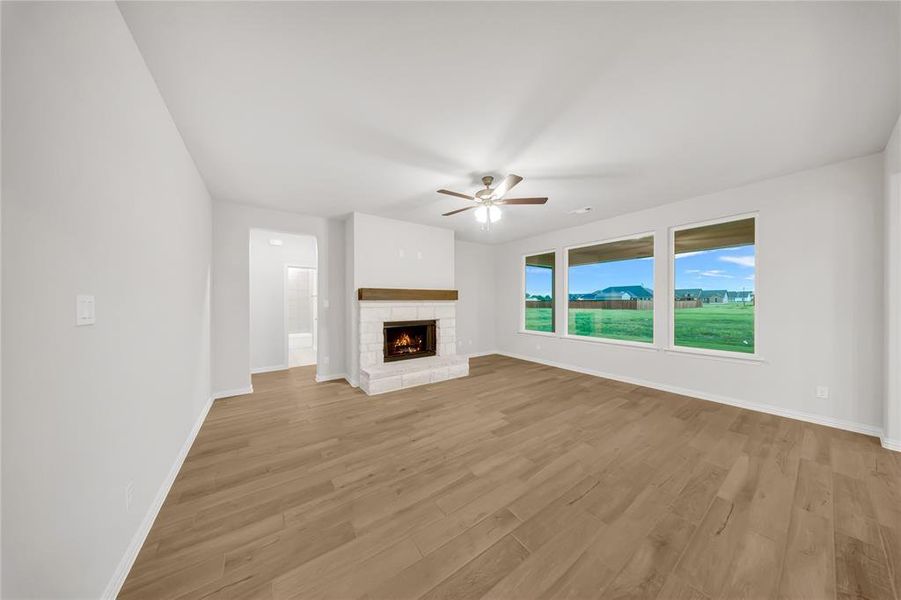 Unfurnished living room featuring a ceiling fan, light wood-type flooring, and a stone fireplace Unfurnished living room featuring a ceiling fan, light wood-type flooring, and a stone fireplace