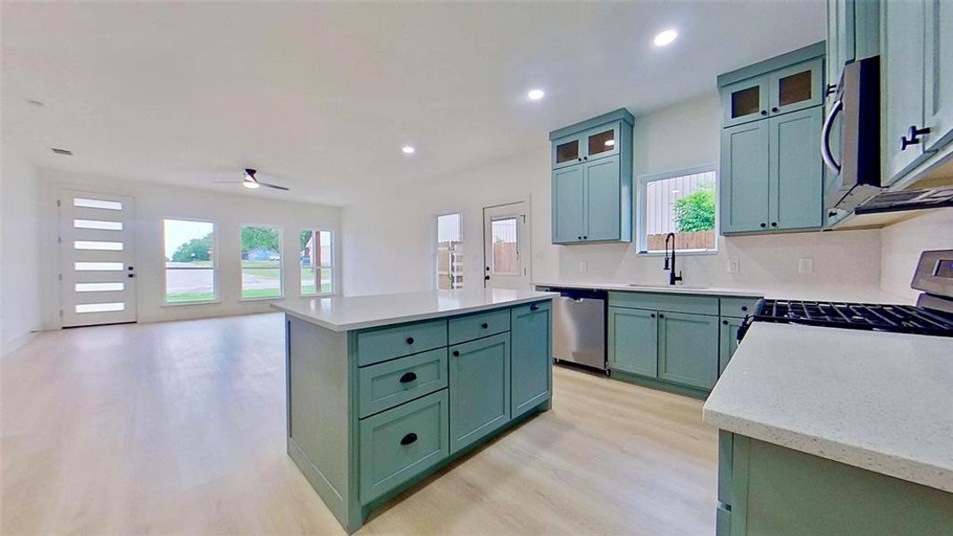 Open-concept living area featuring light wood-finish flooring, a modern ceiling fan, and multiple windows