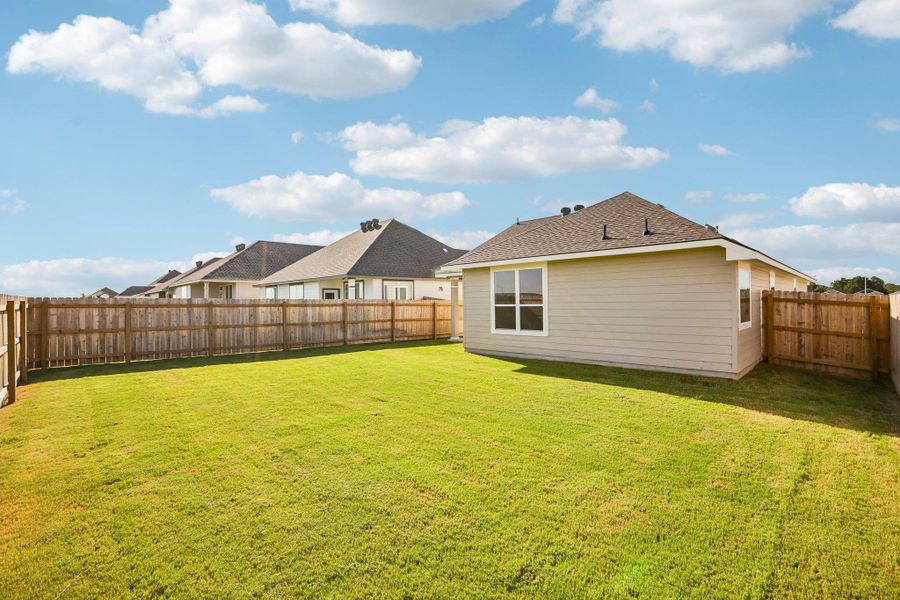 An expansive green lawn sits enclosed by a wooden privacy fence under blue skies.