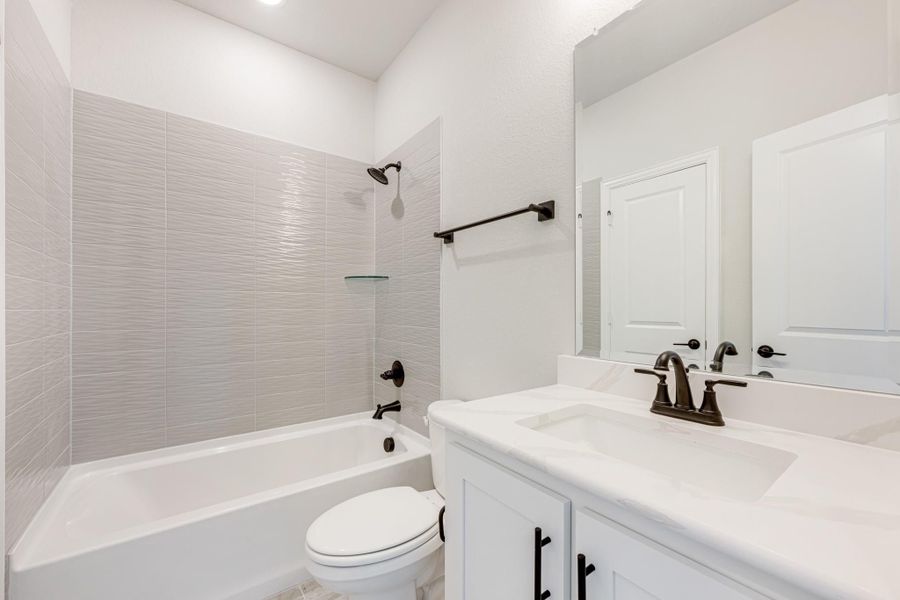 Bathroom with tub-shower combo, gray tile surround, white vanity with dark bronze fixtures, and toilet Bathroom with tub-shower combo, gray tile surround, white vanity with dark bronze fixtures, and toilet