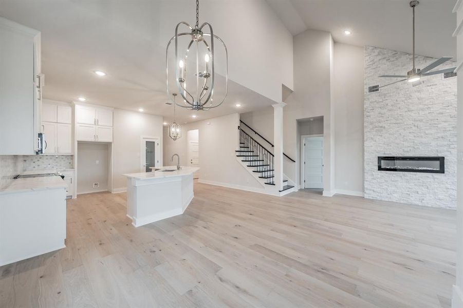 Kitchen featuring a kitchen island with sink, open floor plan, high vaulted ceiling, a stone fireplace, and white cabinets