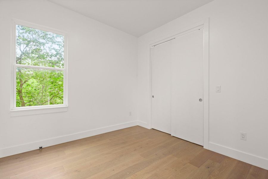Bright room featuring a large double-hung window, light wood-finish flooring, white walls, white baseboards, and a sliding closet door