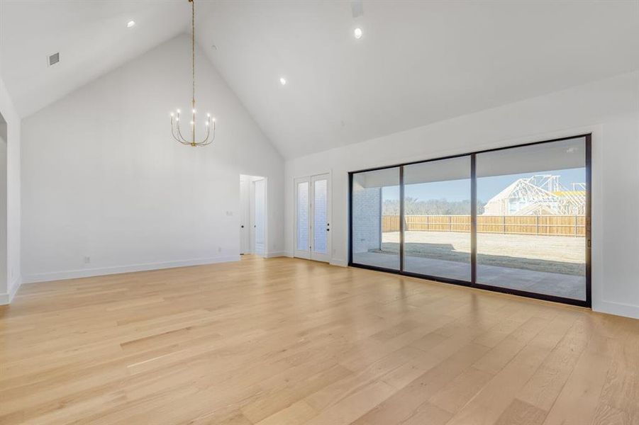Unfurnished living room with a high ceiling, light wood finished floors, and suspended lighting