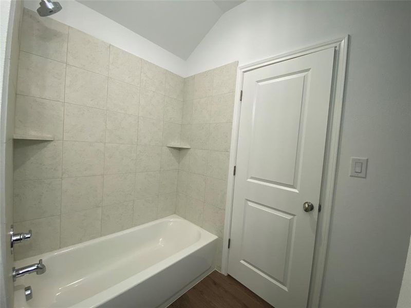 Full bathroom with dark wood-type flooring, lofted ceiling, and shower / bath combination Full bathroom with dark wood-type flooring, lofted ceiling, and shower / bath combination