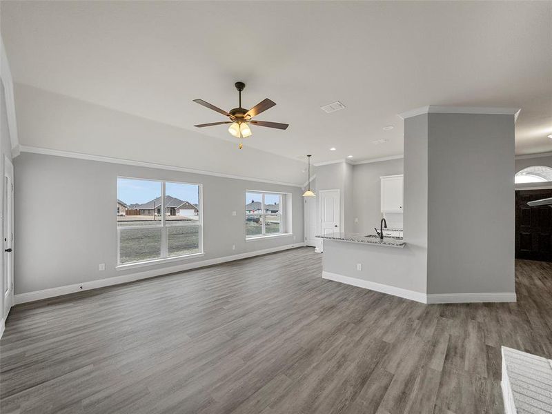 Unfurnished living room featuring visible vents, baseboards, ornamental molding, wood finished floors, and a ceiling fan