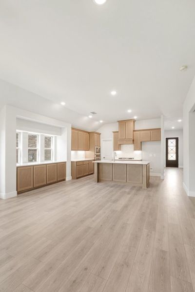 Open-concept kitchen with light wood cabinets, center island, and light hardwood floors in a new construction home.