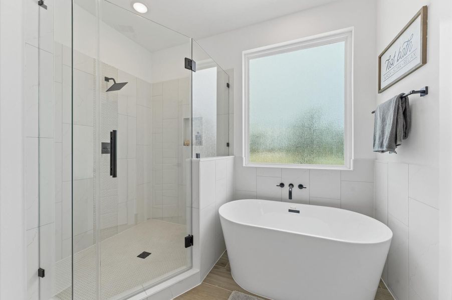 Indulge in everyday luxury in this elegant primary bathroom, where a freestanding soaking tub and a spacious walk-in shower offer the best of both worlds. The frameless glass shower enclosure beautiful tilework, while the tub invites relaxation. A double vanity with quartz countertops and individual mirrors adds modern sophistication, and soft neutral tones create a serene, spa-like ambiance that elevates your daily routine.