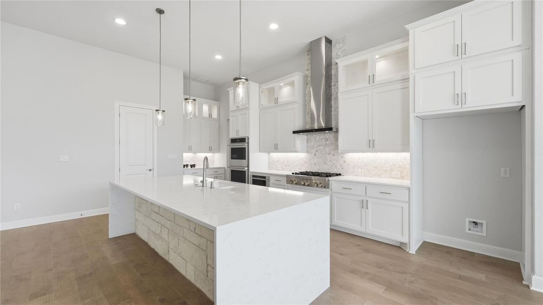 Kitchen with glass insert cabinets, white cabinets, a kitchen island with sink, light stone counters, and light wood-style flooring Kitchen with glass insert cabinets, white cabinets, a kitchen island with sink, light stone counters, and light wood-style flooring
