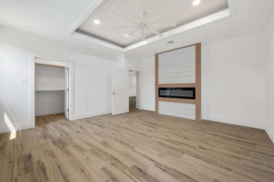 Bedroom featuring a raised ceiling, wood tiled floors, recessed lighting, and a fireplace Bedroom featuring a raised ceiling, wood tiled floors, recessed lighting, and a fireplace