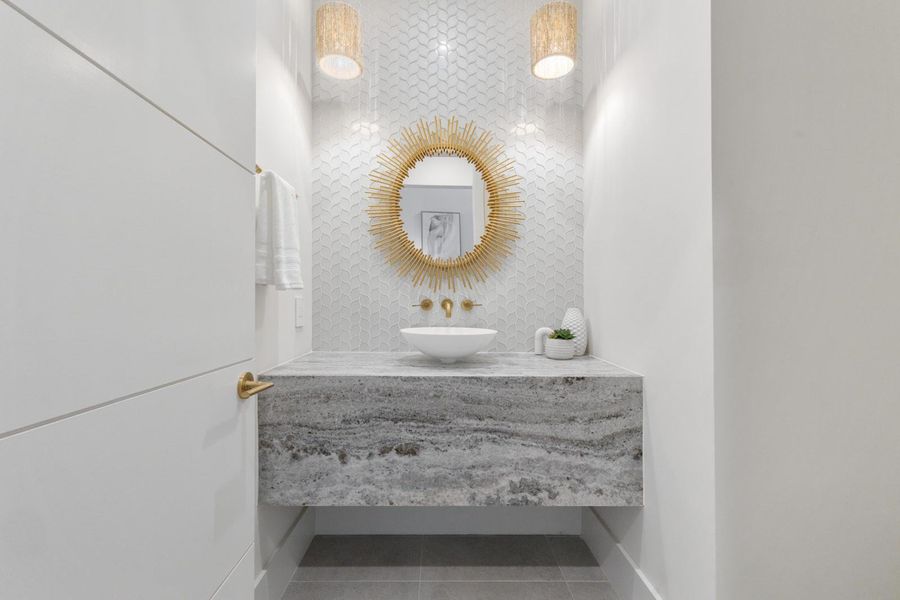 The bathroom features a vessel sink, a vanity with a natural stone countertop, a decorative mirror, and wall-mounted light fixtures