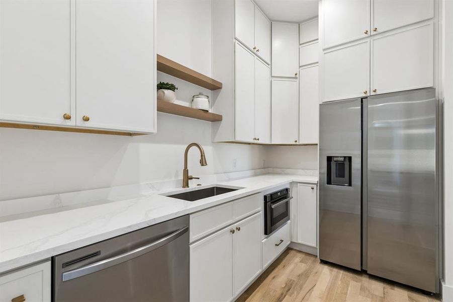 Kitchen featuring stainless steel appliances, open shelves, light wood-type flooring, white cabinetry, and light stone counters