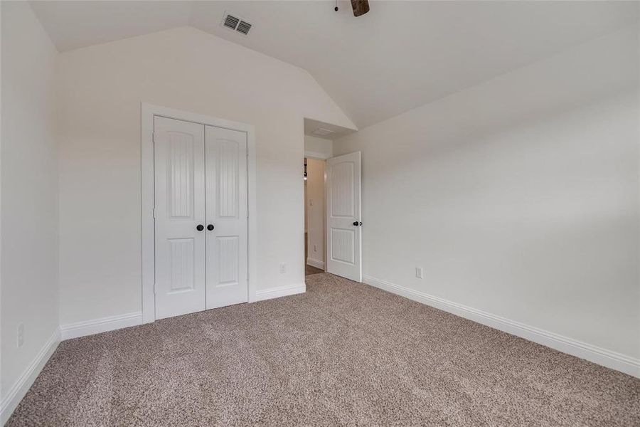 Unfurnished bedroom featuring vaulted ceiling, carpet floors, a closet, and ceiling fan