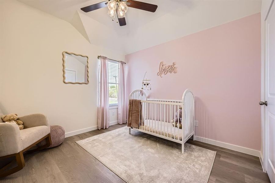 Bedroom featuring a nursery area, vaulted ceiling, wood finished floors, and ceiling fan