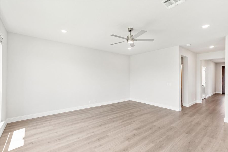 Empty living room with light wood floors, white walls, and a ceiling fan with light fixture