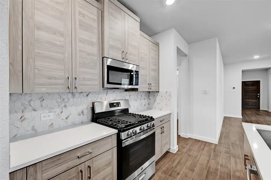Kitchen featuring stainless steel appliances, wood finished floors, backsplash, recessed lighting, and light countertops Kitchen featuring stainless steel appliances, wood finished floors, backsplash, recessed lighting, and light countertops