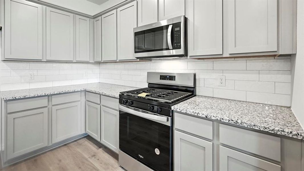 Modern kitchen featuring light gray shaker-style cabinetry, speckled countertops, and a white subway tile backsplash