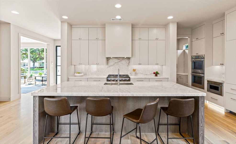 Kitchen with stainless steel double oven, backsplash, light wood-type flooring, a kitchen bar, and recessed lighting Kitchen with stainless steel double oven, backsplash, light wood-type flooring, a kitchen bar, and recessed lighting