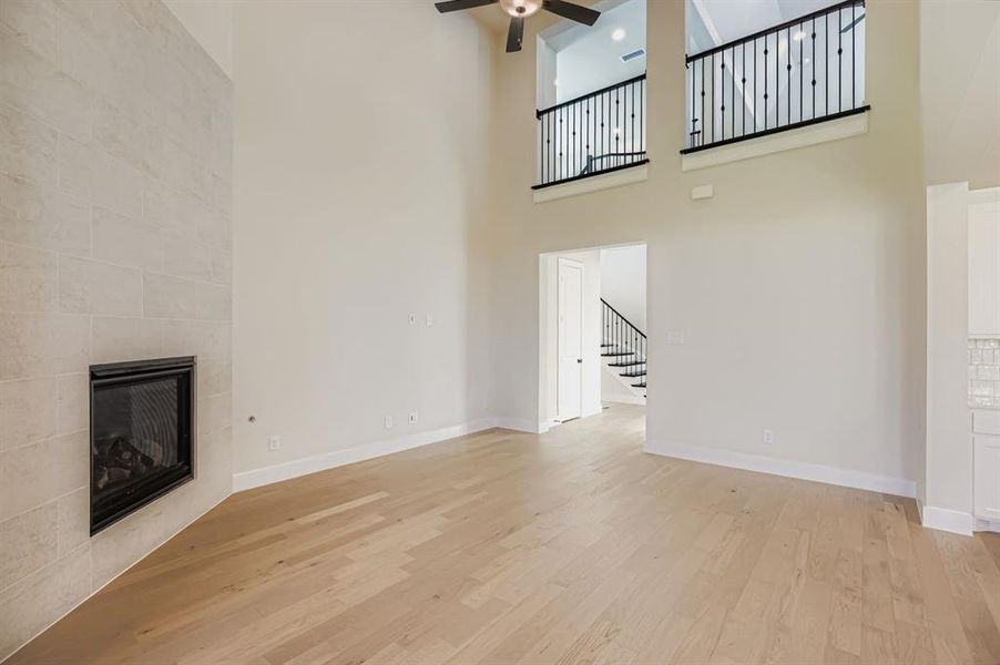 Unfurnished living room with a fireplace, light wood-type flooring, a high ceiling, stairs, and a ceiling fan
