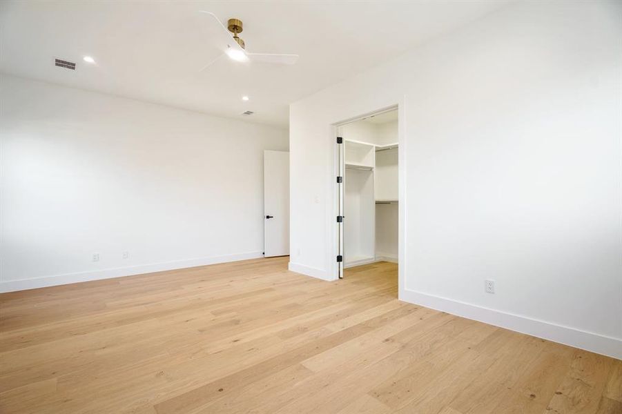 Unfurnished bedroom with a walk in closet, light wood-type flooring, ceiling fan, and a closet