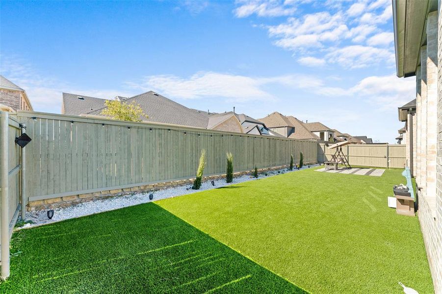 The property features a spacious backyard with artificial turf, a light-colored privacy fence, and a decorative rock border with plantings