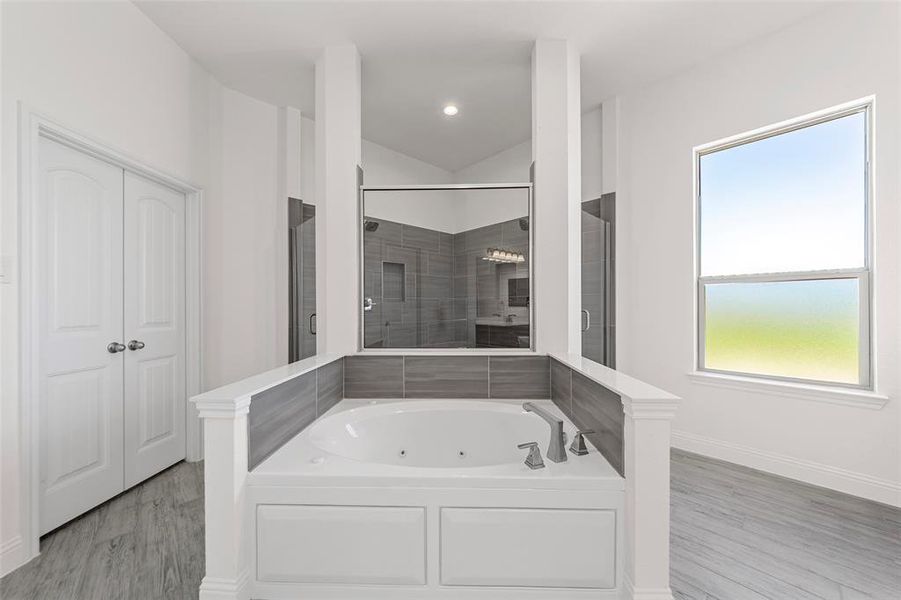 Bathroom with a stall shower, a tub with jets, baseboards, lofted ceiling, and wood finished floors