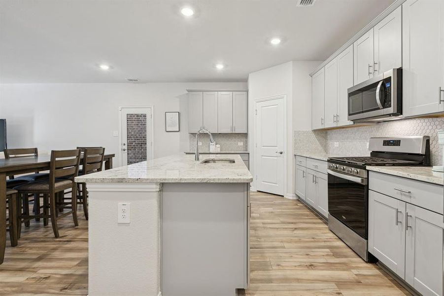 Kitchen with appliances with stainless steel finishes, light stone countertops, an island with sink, light wood-type flooring, and recessed lighting