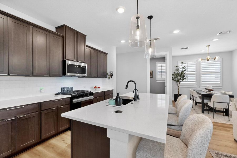 Kitchen with an island with sink, light wood-type flooring, dark brown cabinetry, decorative backsplash, and recessed lighting