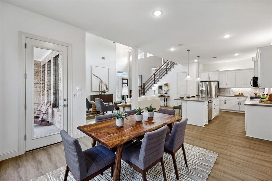 Open-concept living space featuring wood-finish flooring, a contemporary kitchen with white cabinetry and stainless steel appliances, and a dining area with a wood table
