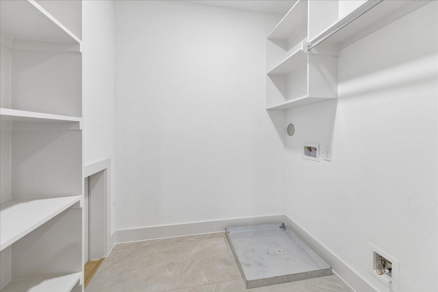 Dedicated utility room provides built in shelving and space for a full size washer and dryer.