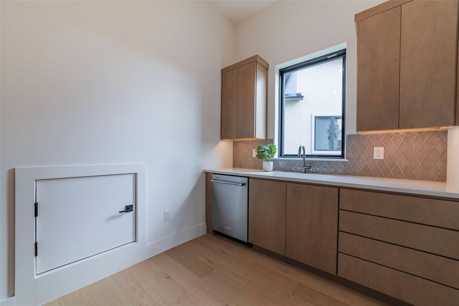 Kitchen featuring light wood-style floors, tasteful backsplash, stainless steel dishwasher, modern cabinets, and light stone countertops