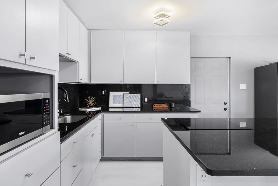 Kitchen with stainless steel microwave, white cabinetry, dark stone countertops, tasteful backsplash, and black electric stovetop