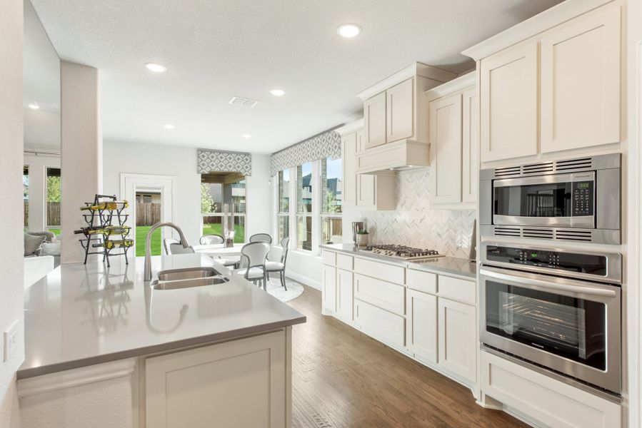 Kitchen with white cabinets, stainless steel appliances, center island, and hardwood floors open to dining area with large windows.