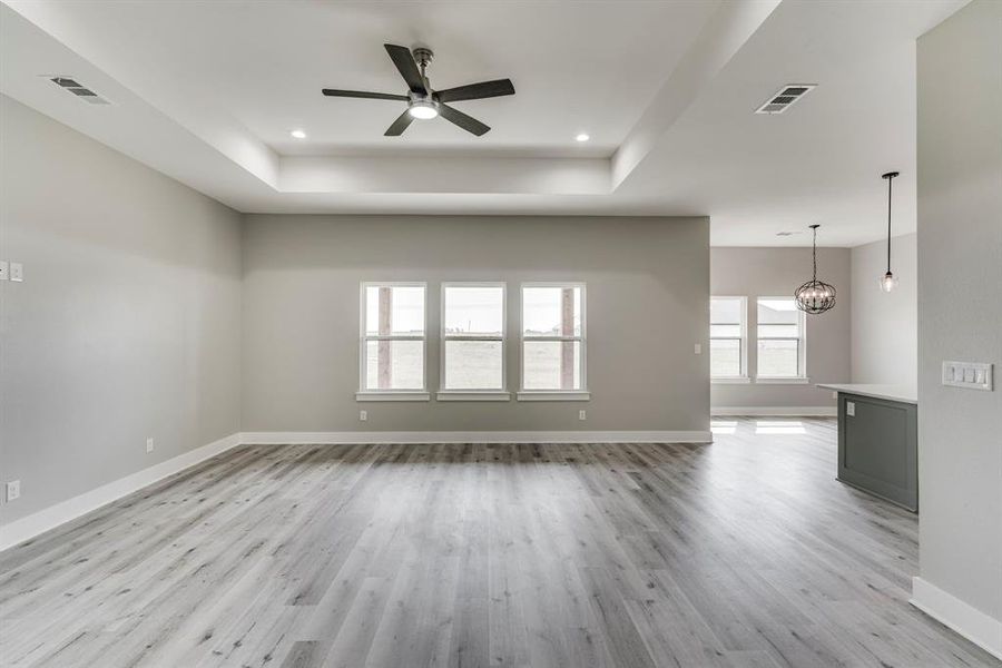 Unfurnished living room with light hardwood / wood-style flooring, a tray ceiling, and ceiling fan with notable chandelier