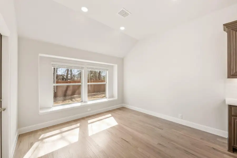 Empty room with vaulted ceiling, light hardwood floors, and double windows with backyard view