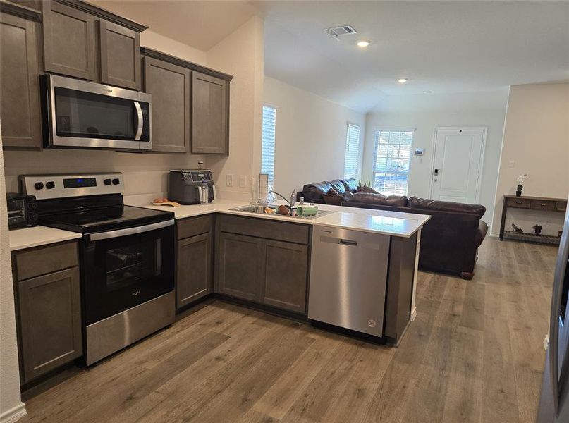 Kitchen with dark brown cabinetry, sink, stainless steel appliances, kitchen peninsula, and hardwood / wood-style flooring